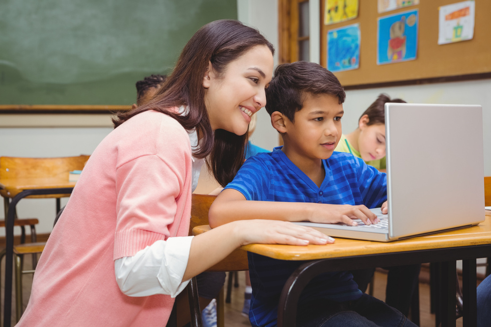 Happy teacher using laptop with student at the elementary school